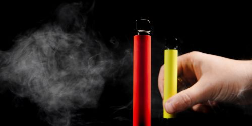 electronic cigarettes of different flavors in hand on a yellow background. The concept of modern smoking, vaping and nicotine.